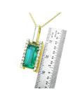 Gold pendant with a baguette cut emerald next to a ruler for scale on a white background.