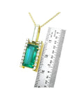 Baguette cut emerald pendant in 18K yellow gold with diamond accents, shown next to a ruler.