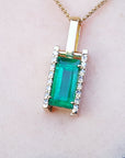 Gold pendant with a genuine emerald on a skin pink background.