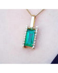 Baguette cut emerald pendant in 18K yellow gold with diamond accents, worn on a neck.