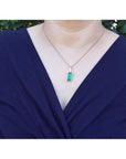 Baguette-cut Colombian emerald pendant in 18K yellow gold with diamonds, worn on a woman's neck.