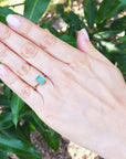 Hand wearing a baguette emerald and side diamonds ring with green leaves in the background.