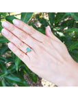 Hand wearing a baguette emerald and side diamonds ring with green leaves in the background.
