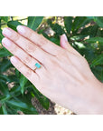 18K yellow gold ring with a baguette-cut emerald and two baguette diamonds on a hand.