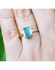 Emerald and side straight baguettes in 18k gold ring on a person's finger against a blurred natural background.
