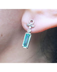Close-up of a emerald baguette cut earring and diamond accent worn on an ear.