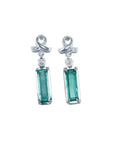 Emerald-cut natural emerald earrings in 14k white gold with diamond ribbon design.