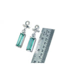 Emerald-cut 1.89 ct. natural emerald earrings in 14k white gold with ribbon design and accent diamonds.