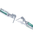 Emerald-cut natural emerald earrings in 14k white gold with ribbon design and accent diamonds.
