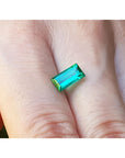 1.62 ct. baguette-cut loose natural emerald, vibrant green, held between fingers.