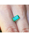 1.62 ct. baguette-cut loose natural emerald, vibrant green, held between fingers.