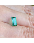 1.62 ct. baguette-cut loose natural emerald, vibrant green, held on a finger.