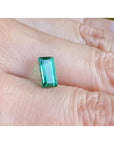 1.62 ct. baguette-cut loose natural emerald, vibrant green, held on a finger.