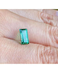 1.62 ct. baguette-cut loose natural emerald, vibrant green, held on a finger.