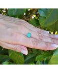 1.62 ct. baguette-cut loose natural emerald, vibrant green, held on a hand against foliage.