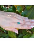 1.62 ct. baguette-cut loose natural emerald, vibrant green, on a hand against green leaves.