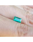 Vibrant green 1.10 ct. baguette-cut loose Colombian emerald gemstone held on a hand.
