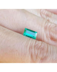 Vibrant green 1.10 ct. baguette-cut loose Colombian emerald gemstone held on a hand.