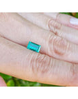 Vibrant green 1.10 ct baguette cut loose Colombian emerald held between two fingers.