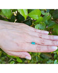 1.10 ct. baguette cut loose Colombian emerald, vibrant green, held on a hand against green foliage.