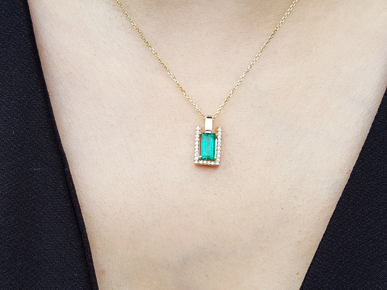 Gold necklace with a natural emerald pendant on a person's neck