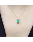 Baguette emerald and diamond pendant necklace in 14K yellow gold, worn on a neck.
