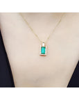 Baguette emerald and diamond pendant necklace in 14K yellow gold, worn on a neck.