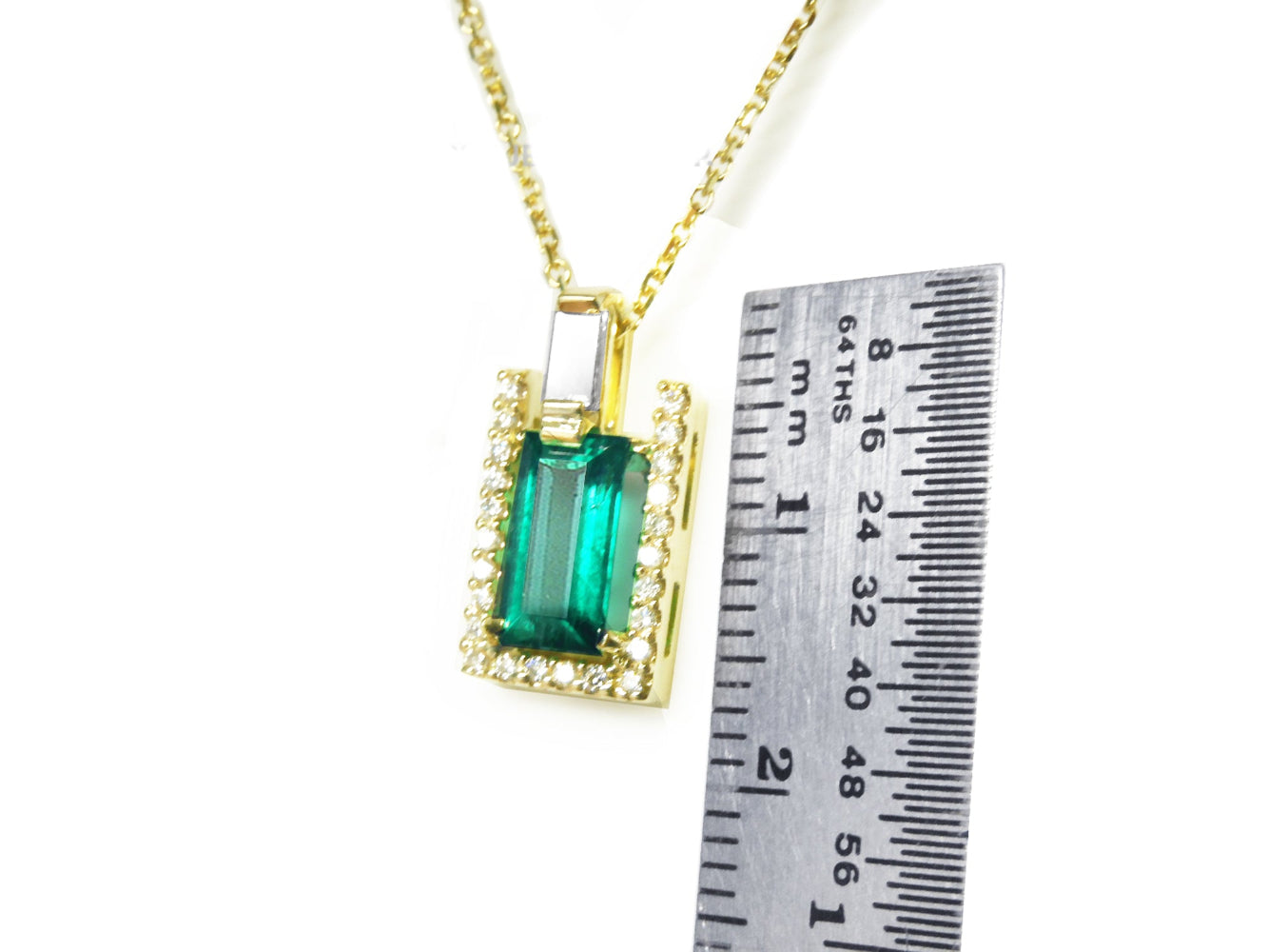 Gold necklace with a natural colombian emerald baguette cut pendant next to a ruler for scale on a white background