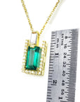 Gold necklace with a natural colombian emerald baguette cut pendant next to a ruler for scale on a white background
