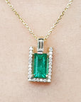 Emerald baguette pendant with diamond accents on a gold chain against a beige skin background.