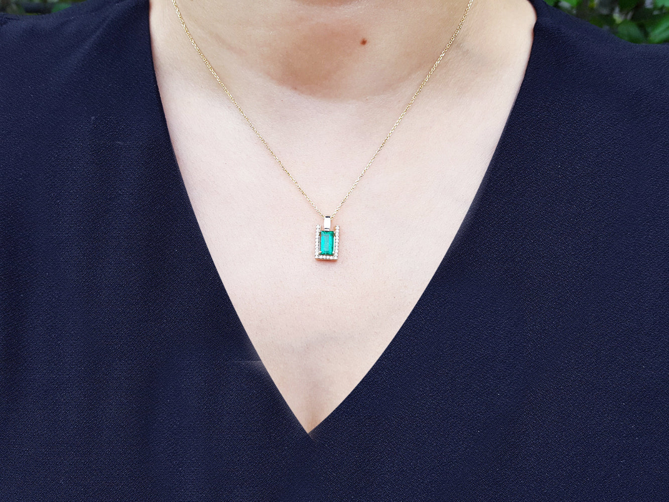 Necklace with a baguette cut emerald pendant worn by a woman in a navy blue top.
