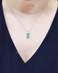 Necklace with a baguette cut emerald pendant worn by a woman in a navy blue top.