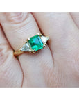A square natural emerald with side trillion diamonds in 18k yellow gold on a hand.