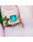 A 14k yellow gold natural colombian emerald ring for men with accent diamonds worn on a finger.