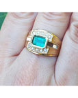 East west style emerald ring for men in yellow gold on a person's finger.
