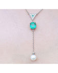 14K white gold necklace with emerald cushion cut, diamond triangle, and hanging white pearl.