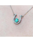 14K white gold horseshoe necklace with a prong-set oval emerald and natural diamonds.