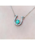 14K white gold horseshoe necklace with a prong-set oval emerald and natural diamonds.