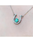 14K white gold horseshoe necklace with a prong-set oval emerald and natural diamonds.