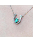 14K white gold horseshoe necklace with a prong-set oval emerald and natural diamonds.
