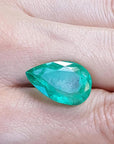 13.42 ct pear-cut Colombian loose emerald with a medium green hue, held in a hand.