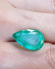 13.42 ct pear-cut Colombian loose emerald with a medium green hue, held in a hand.