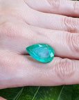 13.42 ct. pear-cut Colombian emerald, medium green, held on a hand over a green leaf.