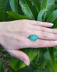 13.42 ct. pear-cut Colombian loose emerald, medium green, held on a hand against green leaves.