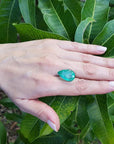 13.42 ct. pear-cut Colombian loose emerald, medium green, held on a hand against green leaves.