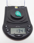 13.42 ct pear-cut Colombian emerald, medium green, on a digital scale displaying its carat weight.