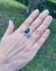 Hand wearing a men's silver ring with a purple Ethiopian black opal against a grassy background