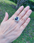 Hand wearing a men's silver ring with a purple Ethiopian black opal against a grassy background