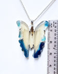 Butterfly-shaped pendant on a chain with a ruler for scale on a white background