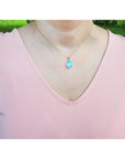 Person wearing a pink top with a necklace featuring a blue opal pendant outdoors.